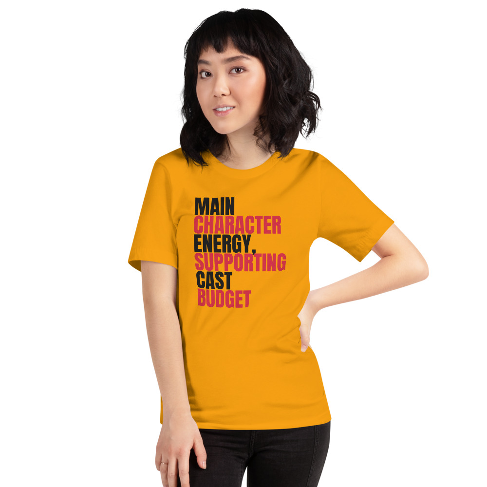 MAIN CHARACTER ENERGY, SUPPORTING CAST BUDGET — printed on a gold t-shirt